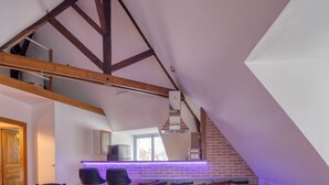 Ein Loft-Zimmer mit freiliegenden Holzbalken, einer Ziegelwand und einer violett beleuchteten Theke.