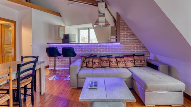 Ein Loft-Wohnbereich mit hohen Decken, freiliegenden Holzbalken, einer Couch, einem Couchtisch und einem Essbereich mit Stühlen und Tisch.