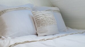 Ein ordentlich bezogenes Bett mit weißer Bettwäsche und zwei Kissen, eines mit Strukturmuster und das andere glatt.