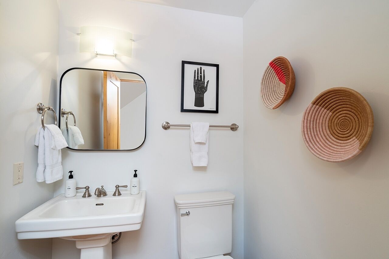 A bathroom with a white sink, a mirror, a framed handprint artwork, a towel rack, and a toilet.