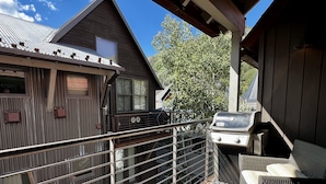 Un balcon doté d’un barbecue, de meubles en osier et offrant une vue sur une maison dont le toit est en métal.