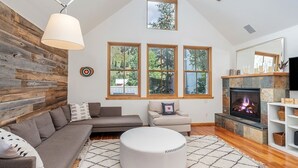 Un salon moderne avec un mur d’accent en bois, une cheminée et de grandes fenêtres donnant sur la forêt.