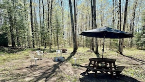 Un montaje para picnic con una mesa, sillas y una sombrilla en un área boscosa.