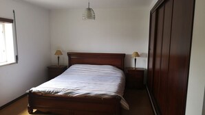 A bedroom with a wooden bed, two bedside tables with lamps, a hanging pendant light, and a wardrobe. - Foz do Arelho in a heavenly setting. (foz do arelho)