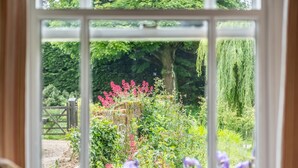 A view through a window with a garden, including a tree, pink flowers, and purple flowers. - Cutbush Farmhouse, Hingham, Norfolk (Hingham)
