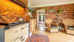 A kitchen with a stove, cabinets, and a brick wall. There is a dining area with wicker chairs and a table. - Cutbush Farmhouse, Hingham, Norfolk (Hingham)
