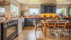A modern kitchen with dark cabinetry, a wooden dining table, and a built-in oven. - Cutbush Farmhouse, Hingham, Norfolk (Hingham)