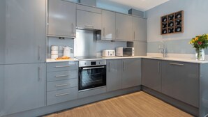 A modern kitchen with grey cabinets, a built-in oven, a microwave, and a sink. - Beautiful 2 Bedroom Apartment With Parking in The Docks (Gloucester)