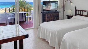 Habitación de hotel con balcón, cama, televisor y escritorio con sillas.