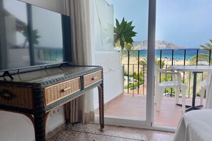 Un balcon avec vue sur la plage et l’océan, un téléviseur posé sur une console, et une chaise blanche.