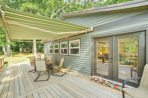 Une terrasse couverte avec une table et des chaises, une terrasse en bois et une maison dotée de grandes fenêtres et d’une porte-fenêtre coulissante.