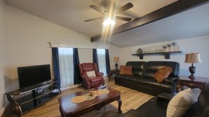 Una sala de estar con televisión, sofá de cuero, sillón y mesa de centro.