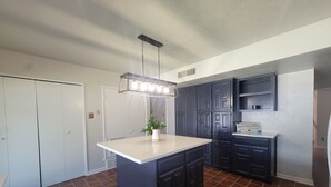 Una cocina con armarios azul marino, encimera blanca y lámpara colgante.