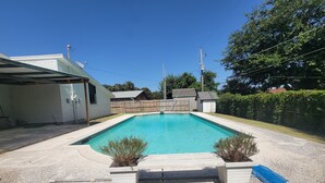 Una piscina rectangular con un borde de baldosas, rodeada por una valla de madera y un área con césped.