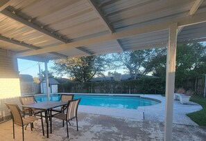 Un patio techado con piscina, una mesa y sillas.