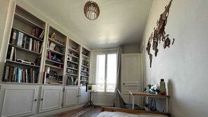 Une chambre à coucher avec un grand lit, un bureau avec une chaise, une bibliothèque et une fenêtre avec des rideaux.