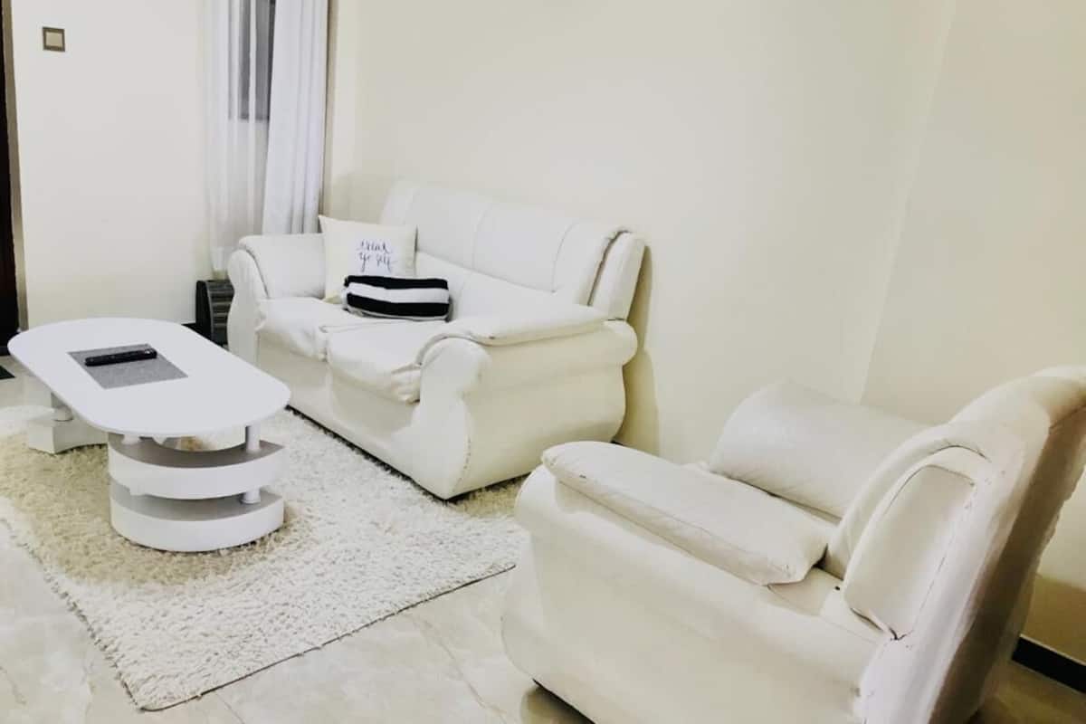 Een moderne woonkamer met een witte bank, een massagetafel en een wit vloerkleed.