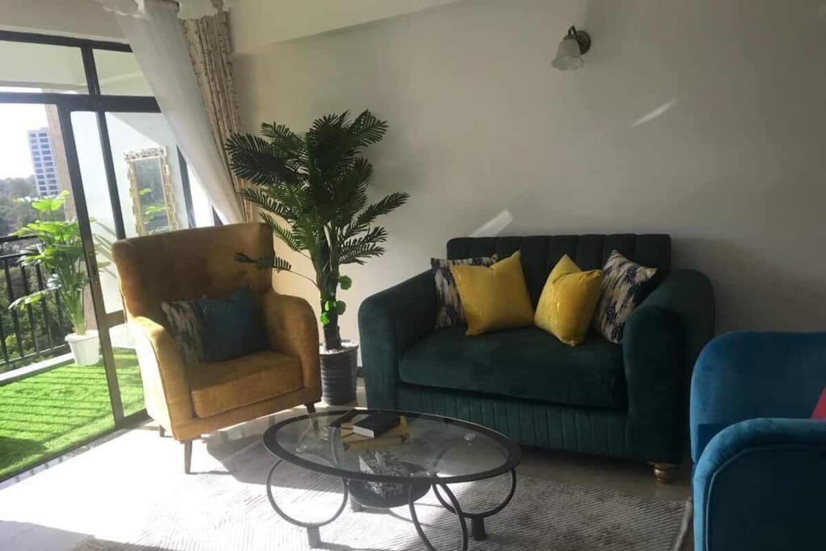 Een woonkamer met een bank, fauteuil en salontafel. Een groot raam biedt uitzicht op groen.