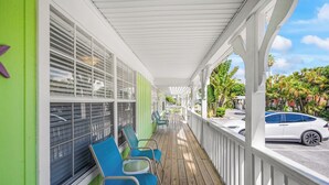 A covered outdoor area with a wooden deck, green walls, and blue chairs. - Romantic Island Getaway! Just Steps from the Beach (Bradenton Beach)