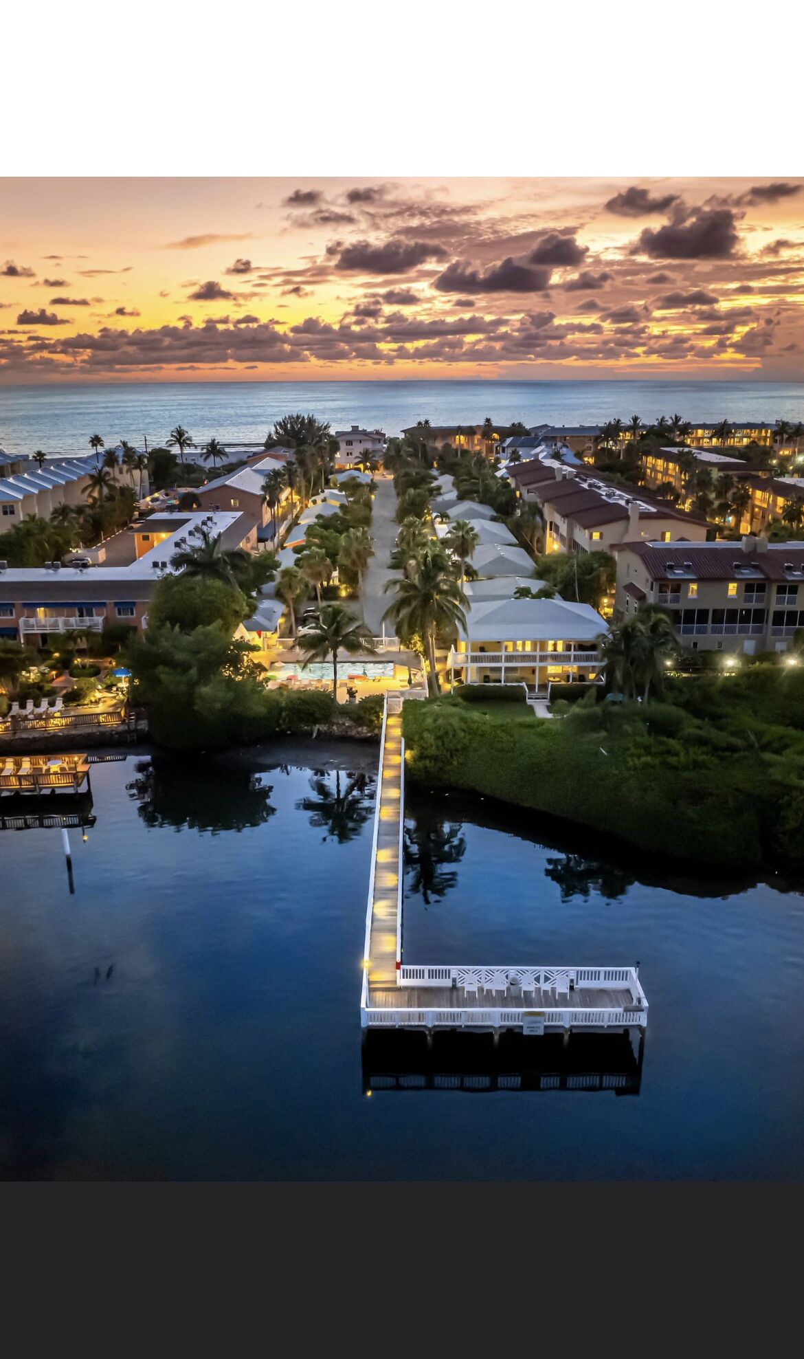 Een luchtfoto van een resort met een centrale pad dat leidt naar een aanlegsteiger boven het water, omringd door gebouwen en palmbomen.
