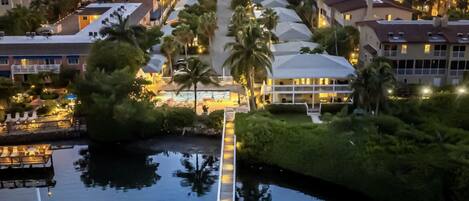 Een luchtfoto van een resort met een centrale pad dat leidt naar een aanlegsteiger boven het water, omringd door gebouwen en palmbomen.