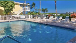 A pool area with lounge chairs, a lifebuoy, and a white fence. - Romantic Island Getaway! Just Steps from the Beach (Bradenton Beach)