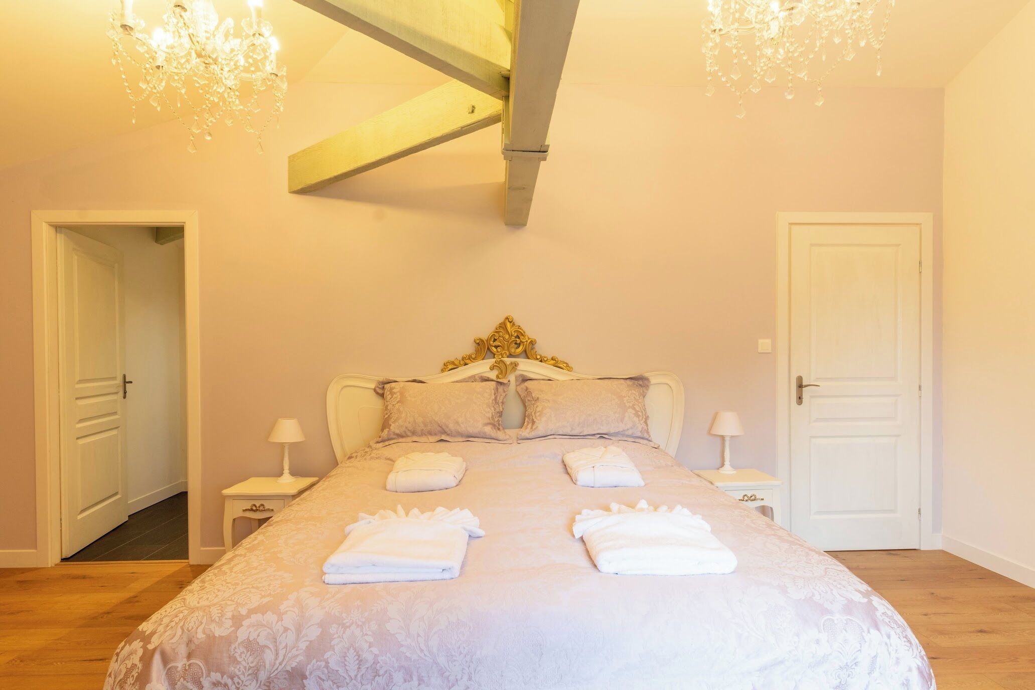 A bedroom with a large bed, two bedside tables, a chandelier, and a door.