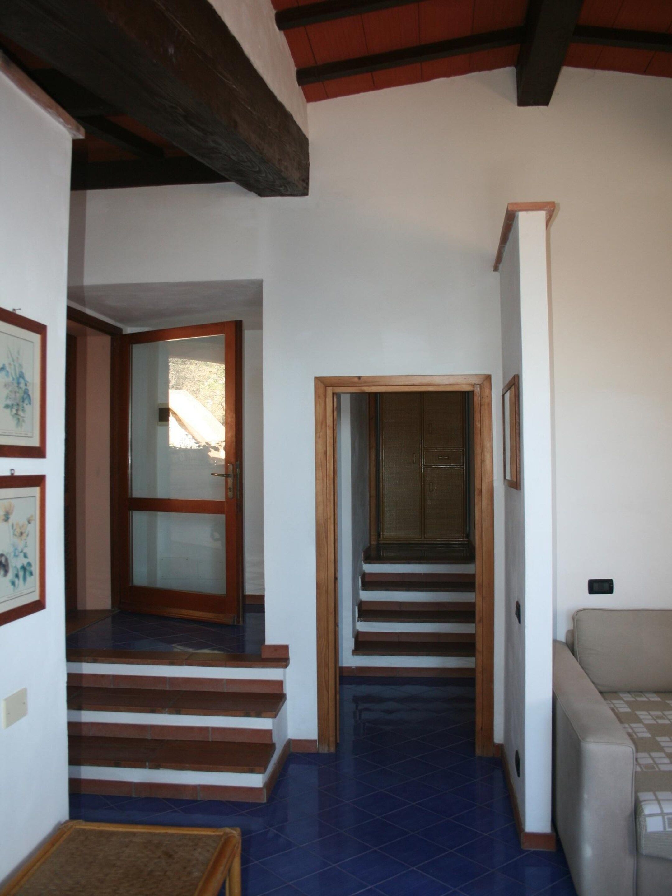 A hallway with a staircase leading to a second floor, a door with glass panels, and a sofa in the foreground.