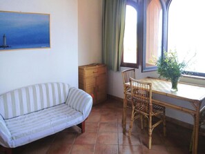 A room with a striped sofa, a wooden cabinet, a dining table with chairs, and a window with curtains. - Holiday Residence La Cota Quinta, Rio Nell"elba (Rio)