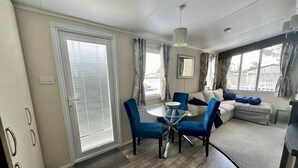 Una sala de estar moderna con una mesa de comedor de vidrio, sillas azules, un sofá beige y un ventanal con cortinas.