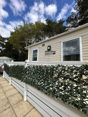 A mobile home with a nameplate reading "Kensington" and a white fence with green foliage. - Caravan - Sleeps 4 - Pool - Pet Friendly (Ringwood)