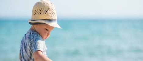 Un enfant joue avec des jouets sur une plage de sable, avec l’océan en arrière-plan.