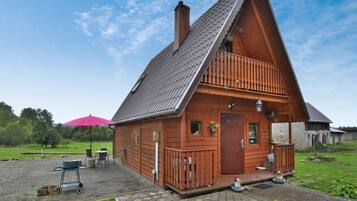 A wooden cabin with a sloped roof, a porch with a railing, and a small garden area with a paved walkway.