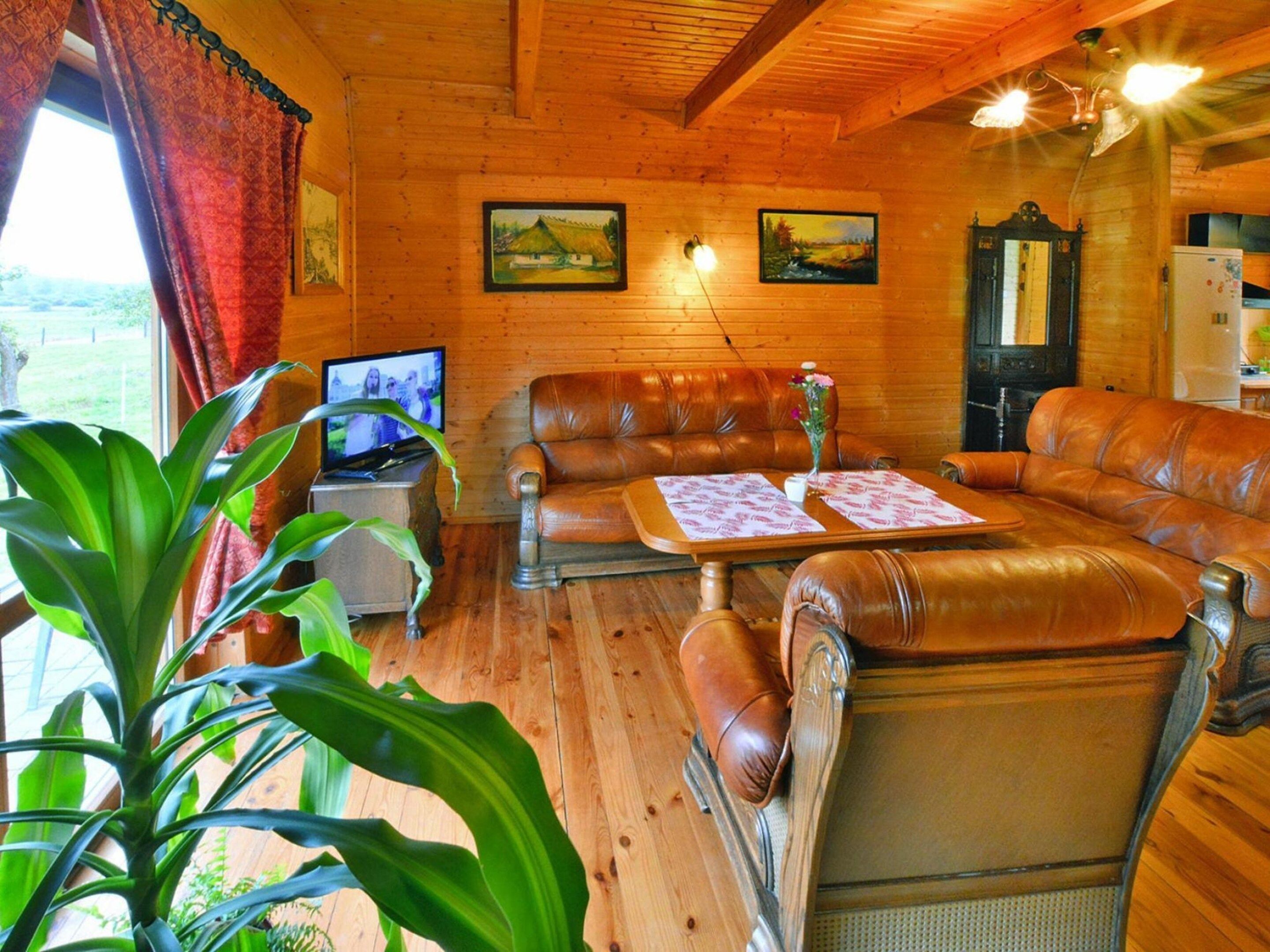 A wooden interior with leather sofas, a television, and a dining table.