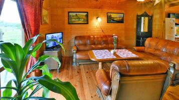 A wooden interior with leather sofas, a television, and a dining table.