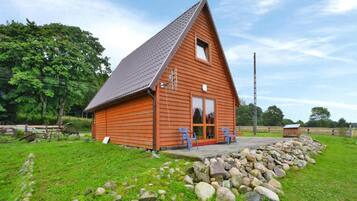 A wooden cabin with a sloped roof, a porch with two chairs, and a stone wall in front.