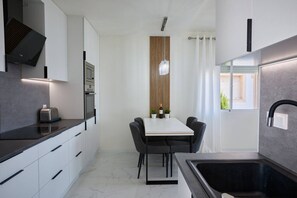 A modern kitchen with a built-in oven, a toaster, and a dining area with a table and chairs. - Casa Loresa Silver (Orihuela)