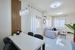 A modern living room with a white sofa, a dining table with chairs, and a large window providing natural light. - Casa Loresa Silver (Orihuela)