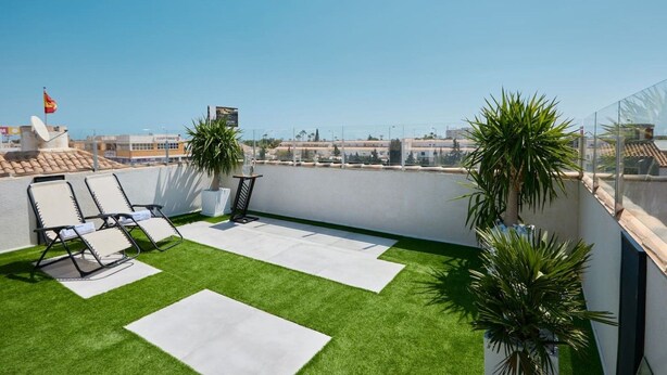 A rooftop terrace with artificial grass, lounge chairs, potted plants, and a clear view of the cityscape. - Casa Loresa Silver (Orihuela)