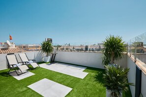 A rooftop terrace with artificial grass, lounge chairs, potted plants, and a clear view of the cityscape. - Casa Loresa Silver (Orihuela)