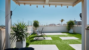 Um terraço no telhado com grama sintética, plantas em vasos e mobiliário de exterior.