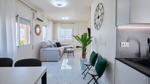 A modern living space with a sofa, dining table, and chairs, a potted plant, and a kitchen area with a sink and countertop. - Casa Loresa Silver (Orihuela)