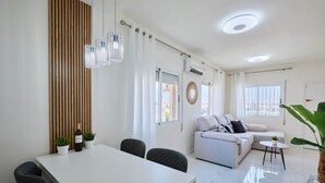 Uma sala de estar moderna com um sofá branco, uma mesa de jantar com cadeiras e uma grande planta em vaso.