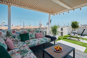 Une terrasse sur le toit avec un canapé, une table garnie de fruits et une vue sur la ville.