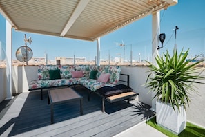 Un espace extérieur aménagé, abrité et doté d’un canapé et d’une table, d’une plante en pot, et offrant une vue sur le paysage urbain.