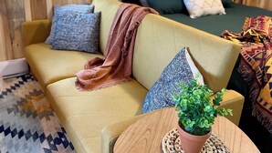 Una habitación acogedora con un sofá, una mesita con una planta, una cama con una manta verde y una ventana con vistas a árboles.