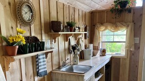 Una cocina rústica con paredes de madera, un lavamanos, un cubo de basura y estantes con utensilios de cocina y plantas.