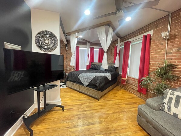 Une chambre à coucher avec un lit, une télévision, un ventilateur de plafond et un mur en briques.