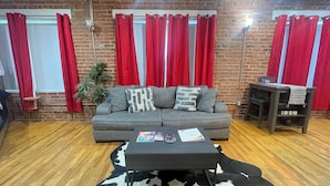 Una sala de estar con un sofá gris, cortinas rojas, una mesa de centro negra y un tapete de cuero de vaca.