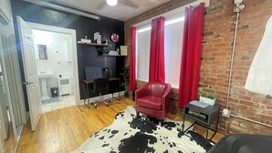 Una habitación con piso de madera, alfombra de cuero blanco y negro, silla de cuero rojo, escritorio con computadora y pared de ladrillo.